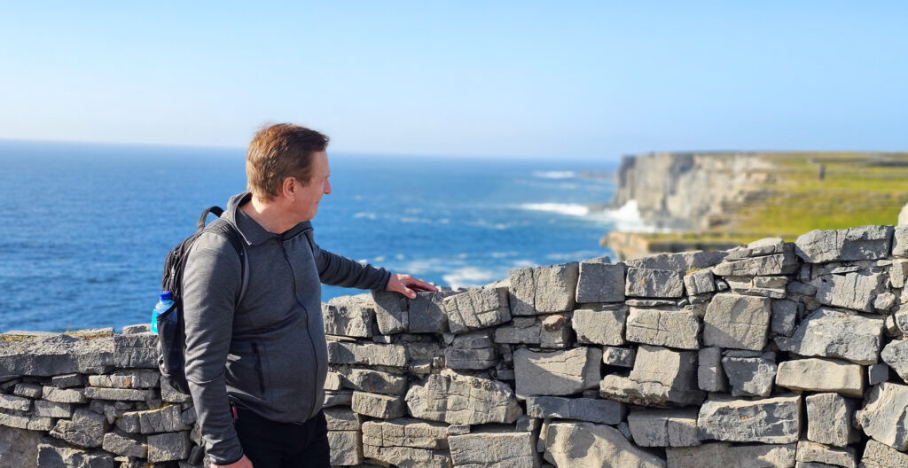 Photo of Karl Johansen standing in front of a wall, looking at the cliffs of Inis Mór, Ireland